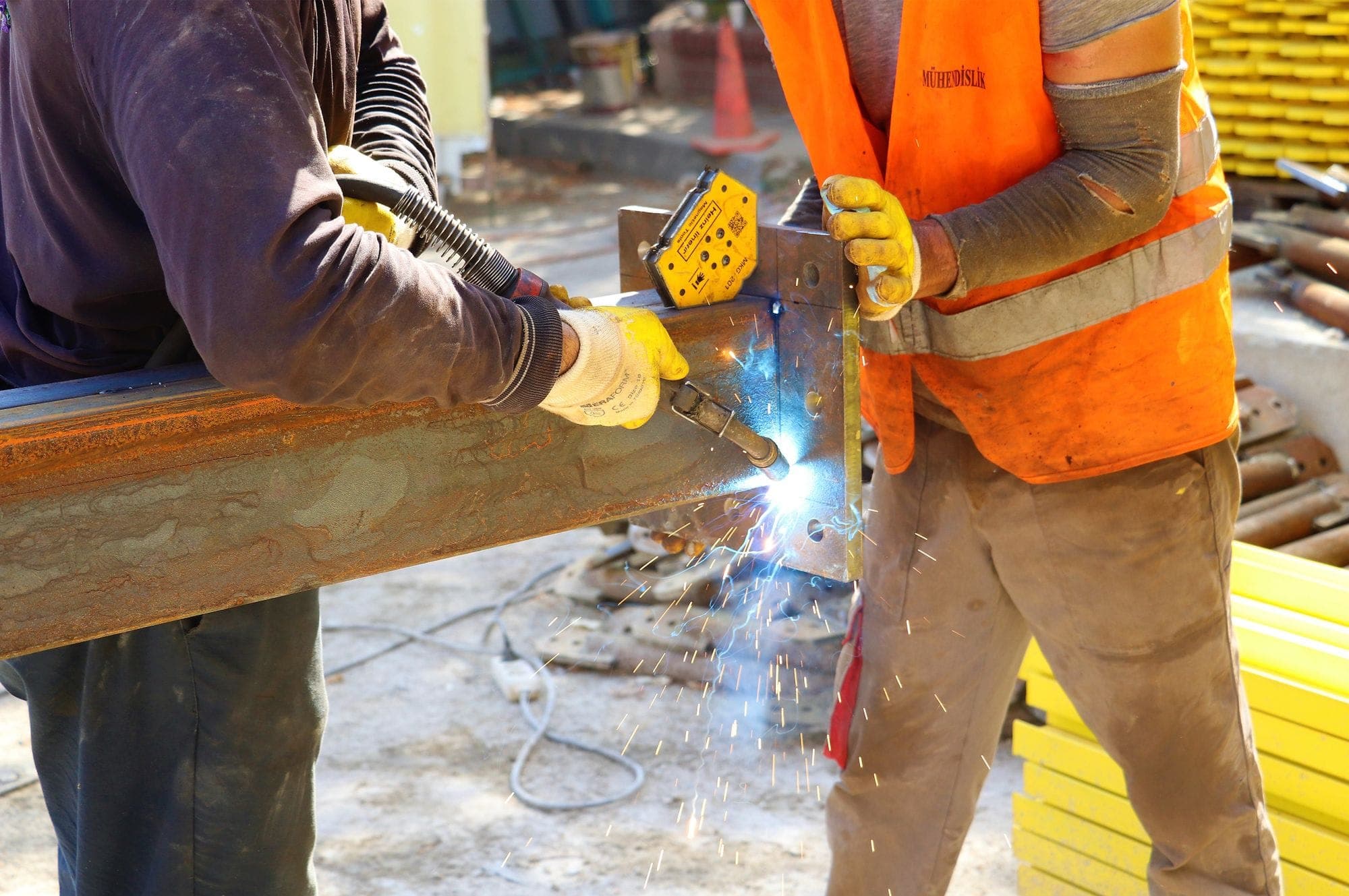 Two workers in safety gear welding steel on a construction site